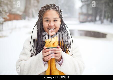 Porträt einer jungen afrikanischen Frau, die beim Trinken die Kamera anlächelt Heißer Tee bei kaltem Wetter Stockfoto
