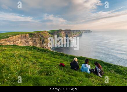 Cliffs off Moher Clare County Ireland Europa drei Mädchen sitzen Auf dem Gras genießen Sie die Aussicht auf die Klippen an einem Sommertag Stockfoto