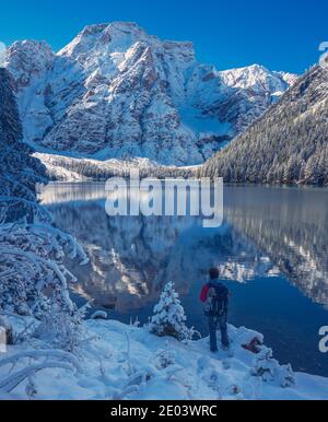 Pragser See Südtirol Italienische Dolomiten Italien Person von hinten Am Ufer eines Bergsees mit Blick auf Schnee Bedeckte Gipfel an einem sonnigen Wintertag Stockfoto