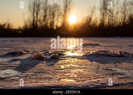 Orange lebhafter Sonnenuntergang auf eisig gefrorenem Hochglanz-See mit geringer Schärfentiefe, langen Schatten. Ausgewählter Fokus und verschwommener Hintergrund Stockfoto