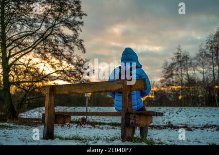 Kidderminster, Großbritannien. Dezember 2020. Wetter in Großbritannien: Mit einem zweiten Tag mit Schneeschauern über Worcestershire endet der Tag mit einem goldenen Winteruntergang, der von einer Dame hier allein auf einer Bank in einem Landschaftspark bewundert wird. Kredit: Lee Hudson/Alamy Live Nachrichten. Stockfoto