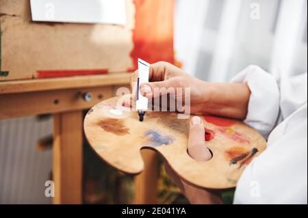 Nahaufnahme der Hand des Künstlers, der die Ölfarbe aus der zusammendrückt Tubus in die Palette Stockfoto