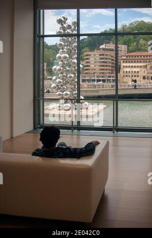 Ruhender Besucher im Museum.Titanwand, Stahlblasen, hoher Baum und das Auge, Skulptur von Anish Kapoor im Guggenheim Museum. Stockfoto