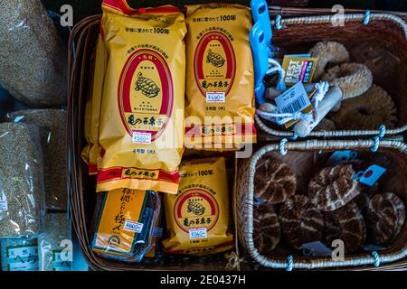 Gelbe Pakete des Scheuerbürstenherstellers Kamenoko Tawashi liegen neben Körben mit getrockneten Pilzen in einem kleinen Feinkostladen. Die traditionelle Bürste mit ihrem Schildkrötenlogo existiert seit 1907. Nihonbashi-Ningyocho, Chuo, Tokio, Japan. Stockfoto