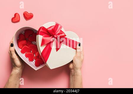 Valentinstag Geschenk in Damen Hand mit roten kleinen Herzen auf rosa Hintergrund. Blick von oben. Flach liegend. Grußkarte mit Kopierplatz. Liebeskonzept. Stockfoto