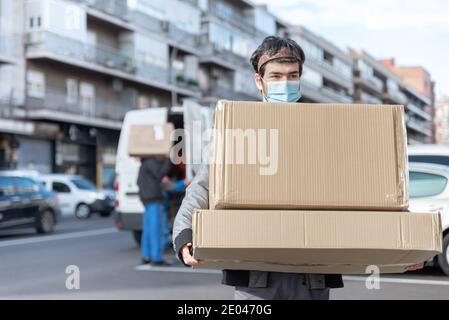 Delivery Mann mit Uniform und Maske trägt eine große Lieferung Box und Van im Hintergrund nicht fokussiert Stockfoto