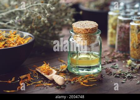 Flasche mit ätherischem Öl, Schale mit trockenen Ringelblumenblättern. Glasflaschen mit Heilkräutern. Alternative Medizin. Stockfoto