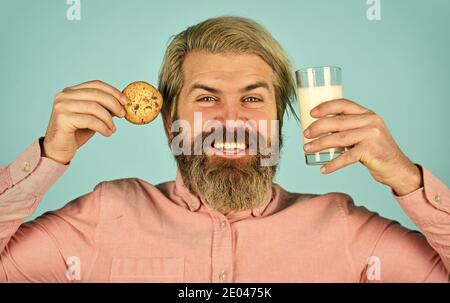 Bärtiger Mann trinkt Milch mit Plätzchen. Lassen Sie es für Santa. Frühstück oder Mittagessen. Milch und süße Kekse. Happy Hipster essen Plätzchen Dessert. Köstliche Leckereien. Hausgemacht ist am besten. Rezept zum Backen von Plätzchen. Stockfoto