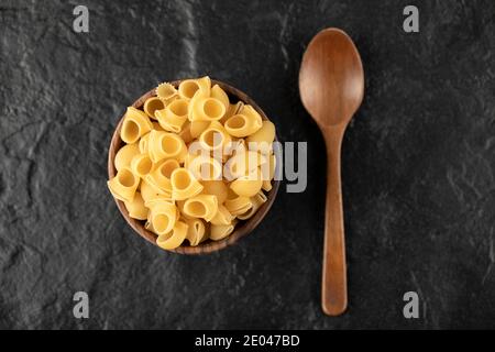 Italienische ungekochte Pasta conchiglie in Holzschale mit einem hölzernen Löffel Stockfoto