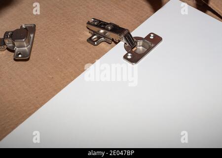 Montage von Holzmöbeln, Metallscharnier an der weißen Schranktür der Kücheneinheit. Zimmermannservice. Stockfoto