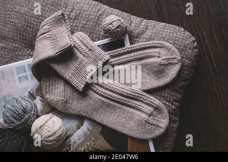 Ein Paar handgestrickte Socken mit Garnkugeln. Natürliche Farben. Dunkler rustikaler Holzhintergrund. Stockfoto