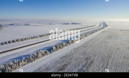 Winterstraße entlang der Felder zwischen den Städten Luftaufnahme von einer Drohne. Winterlandschaft von einer Drohne. Winter Straßenansicht von einer Drohne Stockfoto