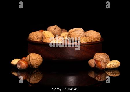 Holzschale mit Walnüssen, Mandeln, Pekannüssen, Haselnüssen in Schale auf schwarzer reflektierender Oberfläche Stockfoto