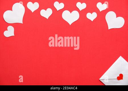 Hintergrund für Valentinstag. Weißer Umschlag und weiße Herzen auf rotem Hintergrund. Stockfoto