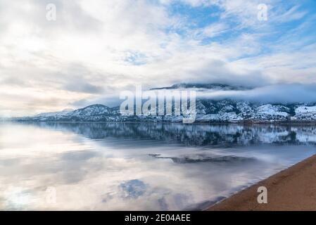 Schneebedeckter Berg, Nebel, Wolken und Sonnenlicht reflektiert in ruhigen See Stockfoto