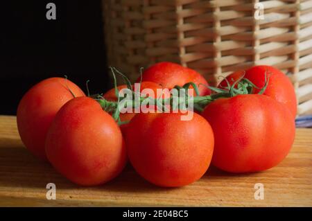 Ein Zweig von Tomaten neben einem Korbkorb auf einem hölzernen Küchentisch, mit Kopieplatz Stockfoto