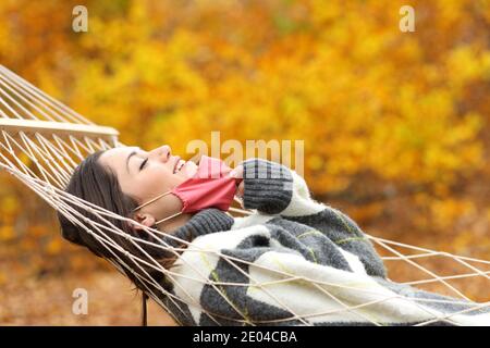 Profil einer glücklichen Frau, die die Schutzmaske abnimmt Frische Luft auf Hängematte im Herbst Stockfoto