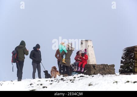 Familie mit Kindern und Hunden am trig Point or Triangulationspunkt auf dem Gipfel der Bosley Cloud bei Congleton Cheshire im Winterschnee Stockfoto