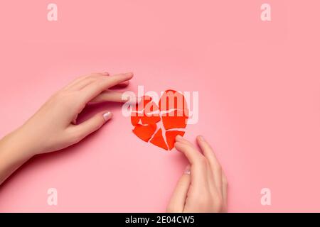 Weibliche Hände kleben zusammen gebrochenes Herz, Stücke von zerrissenen roten valentine auf rosa Hintergrund. Konzept der Enttäuschung in der Liebe, Rettung der Relationsh Stockfoto