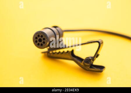 Lavalier- oder Reversiermikrofon auf gelber Oberfläche, sehr nah. Die Details des Griffclips oder BH. Stockfoto