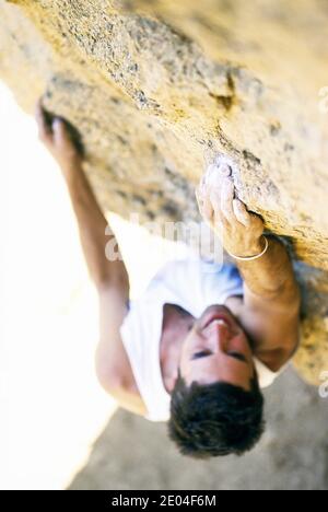 Ein junger Mann klettert im Smith Rock State Park, Oregon. Nach unten schauend und konzentriert auf die Hand, die einen Halt auf der Felswand ergreift. Stockfoto