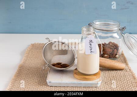 Mandelmilch in einer Flasche neben einem Glas und einem Sieb voller Mandeln. Horizontale Ansicht. Stockfoto