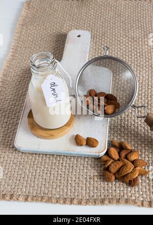 Blick von oben auf Mandelmilch in einer Flasche neben einem Glas und einem Sieb voller Mandeln. Stockfoto