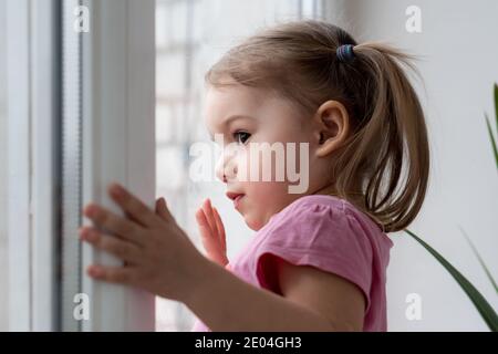 Kindheit, Einsamkeit, Isolation, Traurigkeit, Hoffnung Konzepte - eine traurige niedlich besorgt Kleinkind Baby Mädchen in rosa mit Pferdeschwänze Frisur schaut durch Stockfoto