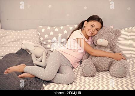 Ideal zum Kuscheln. Glückliches Kind hält Teddybärspielzeug im Bett. Kleine Mädchen spielen mit weichem Spielzeug. Spielwarenladen oder -Geschäft. Kinderspielzeug. Spielzeit. Kindheitsspiele. Stockfoto