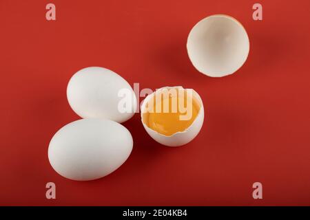 Zerbrochene und ganze rohe Eier auf rotem Hintergrund Stockfoto