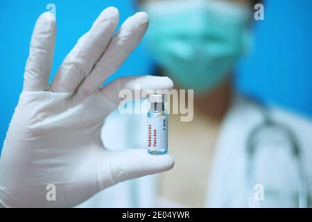 Eine asiatische Ärztin mit OP-Maske und weißen Gummihandschuhen in einer Klinik, hält eine Glasflasche mit 1 Dosis ROTA-Impfstoff mit weißem Hintergrund A Stockfoto