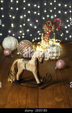 Weihnachtsdekoration - Holzspielzeug Schaukelpferd, Bälle für den Weihnachtsbaum, Silvester Süßigkeiten in einem Glas, umschlitzt mit einer glühenden Girlande auf einem Stockfoto