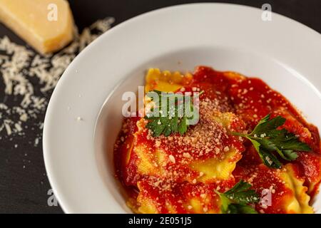 Close up Bild von weißem Porzellan Teller der italienischen Ravioli in Tomatensauce mit geriebenem Parmesan Käse und frischen grünen Petersilienblättern beendet. Ein Chee Stockfoto