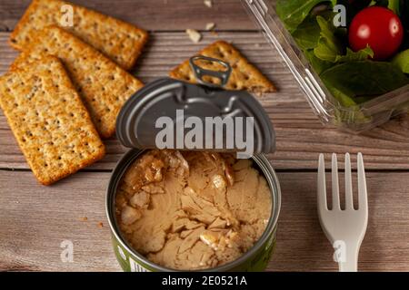 Abgewinkelte Bild von schnell-und Snack-Foto mit einer leicht offenen Dose Thunfisch mit Thunfisch Stücke in Öl auf Holztisch oder Bank, klare Kunststoffbehälter mit Stockfoto