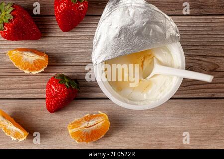 Eine weiße Plastikschale aus reinem griechischem Joghurt mit einem Abgeschälte Aluminiumfolie Dichtung und ein Einweg-Plastiklöffel Eingetaucht serviert mit Mandarinenscheiben A Stockfoto