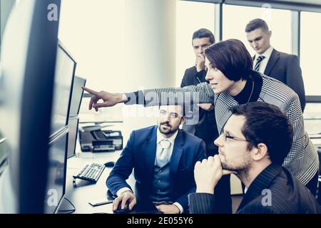 Geschäftsteam, das Daten auf mehreren Computerbildschirmen im Unternehmensbüro betrachtet. Geschäftsfrau zeigt auf dem Bildschirm. Geschäftsleute, die online handeln Stockfoto