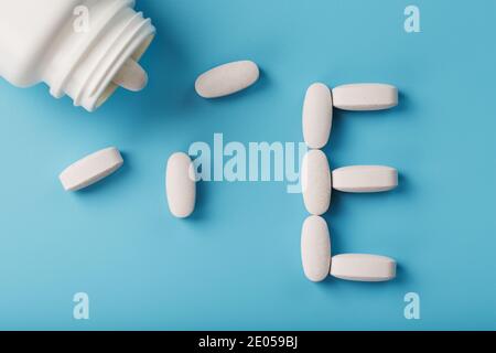 Weiße Kapseln mit Vitaminen in Form von E werden aus einem Glas auf blauem Hintergrund gegossen. Freier Speicherplatz Stockfoto