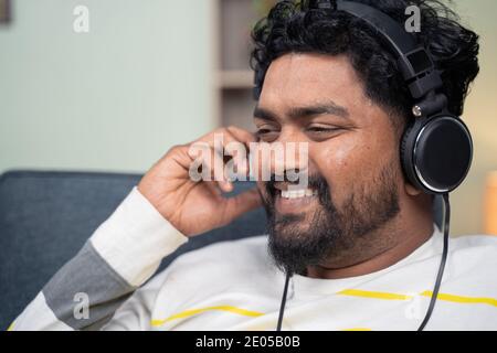 Nahaufnahme des jungen Mannes, der zu Hause friedliche Musik hört, während er auf dem Sofa liegt - Konzept des Musikliebhabers, Entspannung am Wochenende und modern Stockfoto
