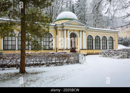 Marianske Lazne, Tschechische Republik - Dezember 29 2020: Winteransicht des neoklassizistischen Waldfrühling-Pavillons mit gelber Fassade, die in einem Park steht. Sno Stockfoto