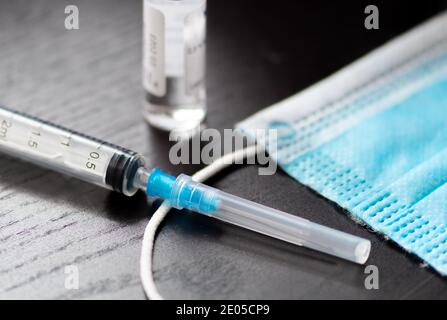 Spritze, Fläschchen und chirurgische Gesichtsmaske auf einem Tisch bereit verwendet werden. Hintergrund des Covid- oder Coronavirus-Impfstoffs Stockfoto