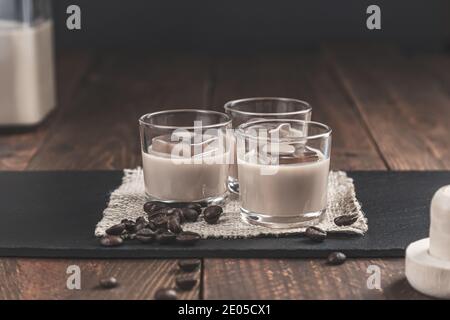 Gläser Sahne-Kaffee-Likör mit Eis und Kaffeebohnen auf rustikalem Holzhintergrund. Stockfoto