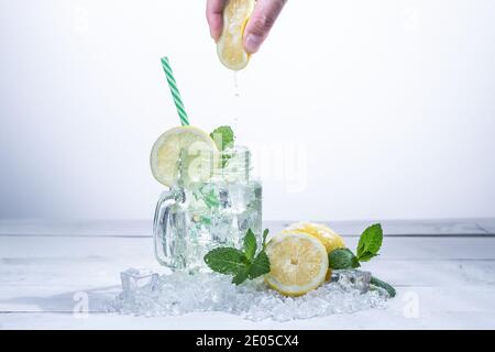 Krug mit sehr erfrischender Limonade mit Zitronen, Minze und Eis, auf weißem Holz mit handgepresster Zitrone Stockfoto