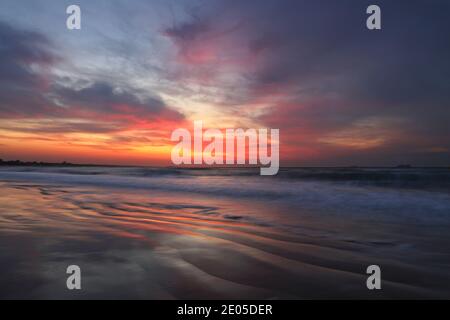 Die Sonne beginnt über dem Meer und Bournemouth Beach aufzugehen. Im Meeresboden sind wellende Linien sichtbar, wenn sich die Wellen zurückziehen. Stockfoto