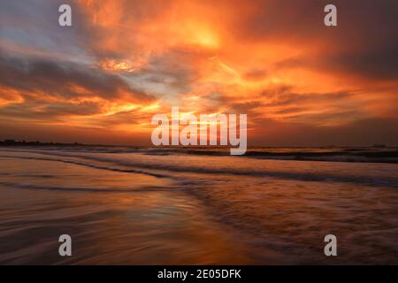 Die aufgehende Sonne brennt am wolkenüberfluteten Himmel, während Wellen über Bournemouth's preisgekrönten Strand Rollen. Stockfoto