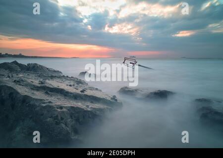 Das Meer wirbelt und stürzt um die Felsen einer Meeresschutzgroyne am Bournemouth Beach, während die aufgehende Sonne durch die Wolkendecke bricht. Stockfoto