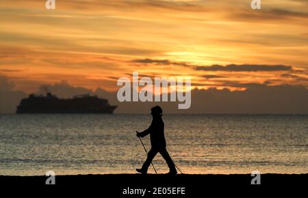 Sandbanks, Großbritannien. Dezember 2020. Ein Spaziergänger nimmt den Sonnenaufgang in ihrem Schritt, wie sie macht hwr Weg entlang des Strandes bei Sandbanks in Poole, Dorset. Quelle: Richard Crease/Alamy Live News Stockfoto