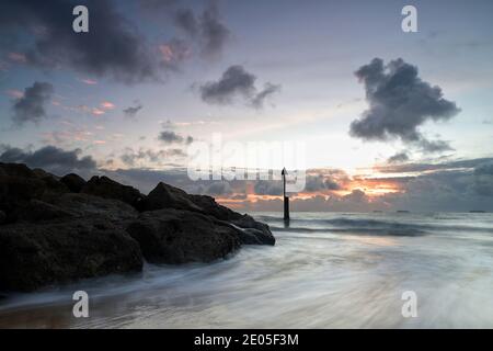 Eine Explosion feuriger Farbe bricht durch die Wolken am Horizont aus, während die Sonne über der ankommenden Flut am Bournemouth Beach aufgeht. Stockfoto