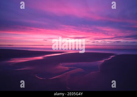 Die aufgehende Sonne füllt den Winterhimmel mit magisch-rosafarbener Farbe über den Gezeitenbecken, die in den feuchten Sand des Bournemouth Beach geätzt sind. Stockfoto