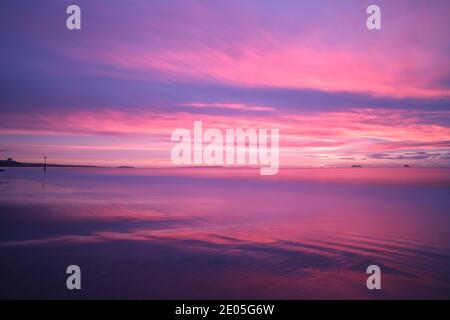 Die Sonne malt die Wolken mit magischen rosa und violetten Farben, während sie an einem kalten Morgen am Bournemouth Beach in einen Winterhimmel aufsteigt. Stockfoto