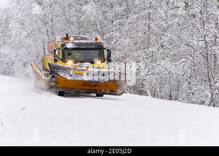 Ein Schneefräsen-Auto räumt an einem Wintermorgen Schnee im Wald von der Straße. Schneepflug LKW Reinigung eisige weiße Straße Stockfoto